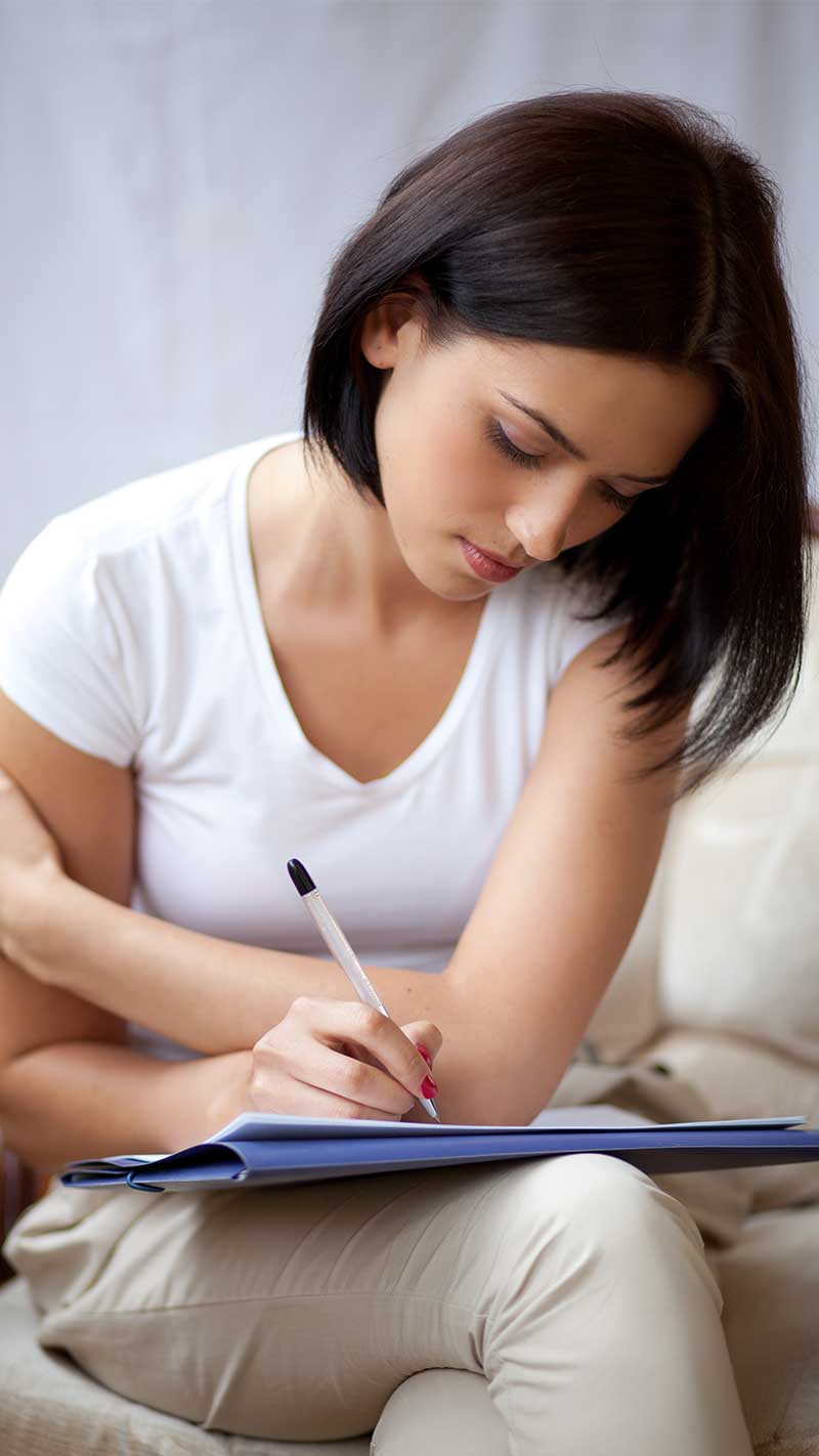 a woman sits with a pen and pad, writing a home inventory