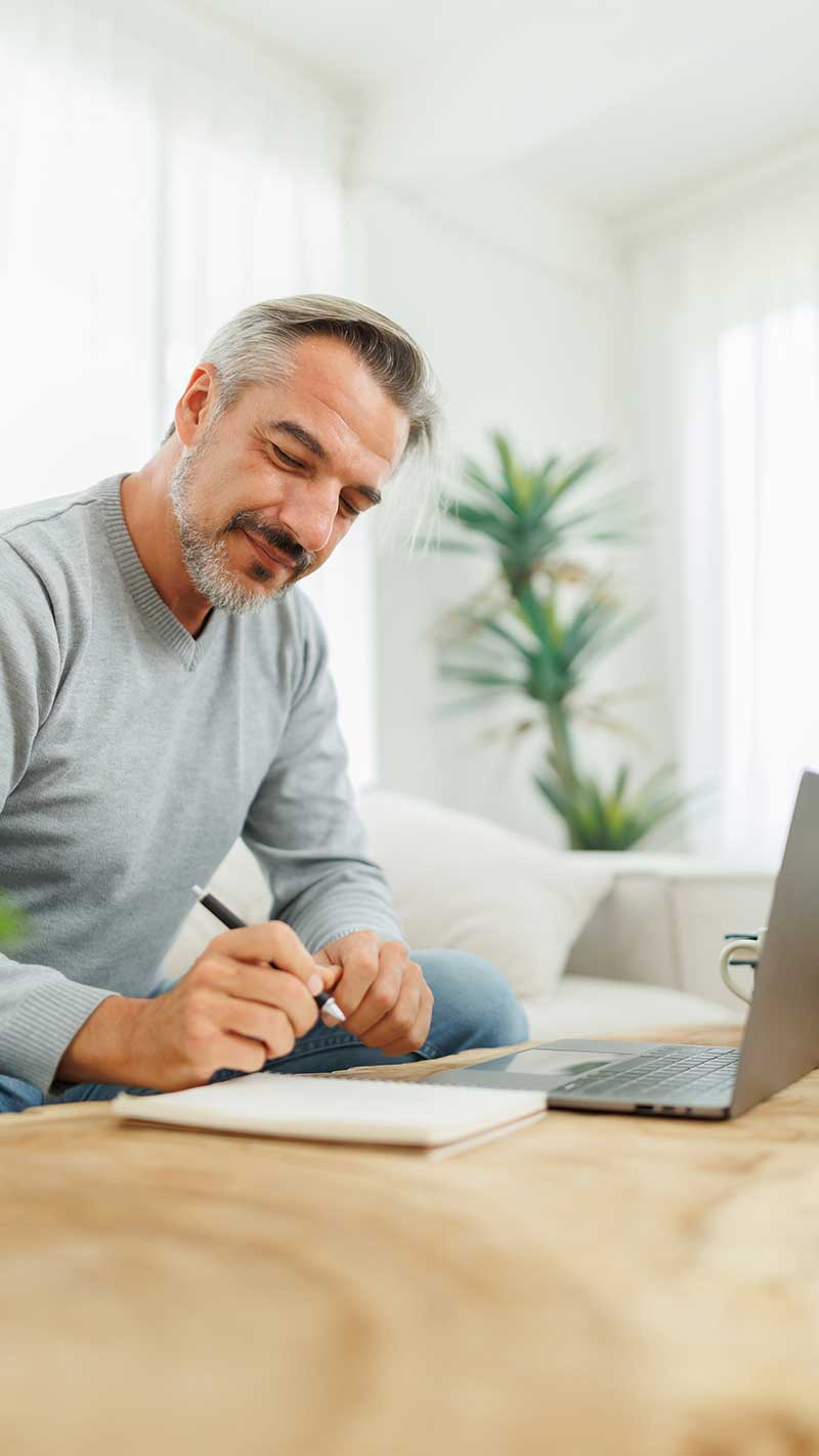 a man sits at a notepad and laptop and does a home inventory